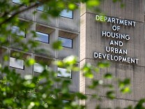 A large concrete building behind some green trees with a sign on the front that says "Department of Housing and Urban Development"
