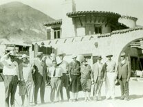 A group of people standing in front of a mansion in the desert.