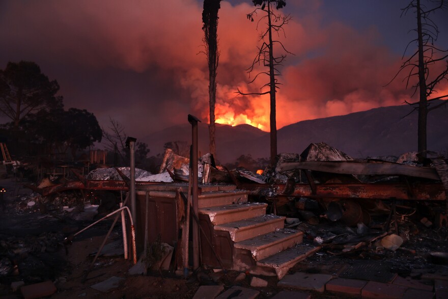 Stairs remain standing at a destroyed trailer home as the Nixon Fire burns in the background.