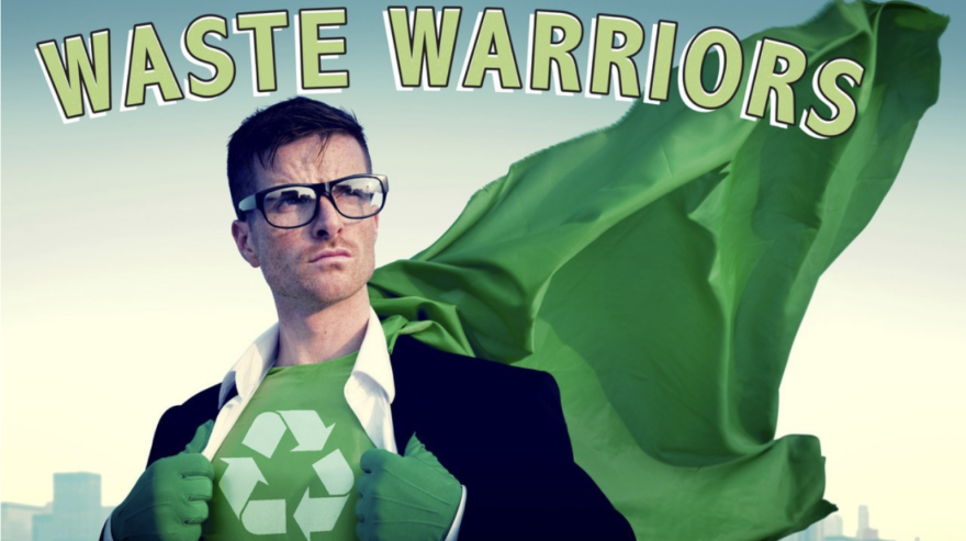 An image of a man wearing a green cape and black-rimmed glasses pulling apart the front of his suit to reveal a green shirt with a recycling symbol.