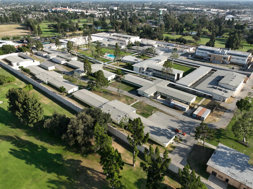 An arial image of a large facility with gray long rectangular buildings and some grassy areas in the center including a pool.