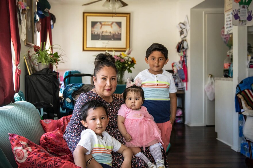A woman sits on the sofa and poses for a photo with her three children.