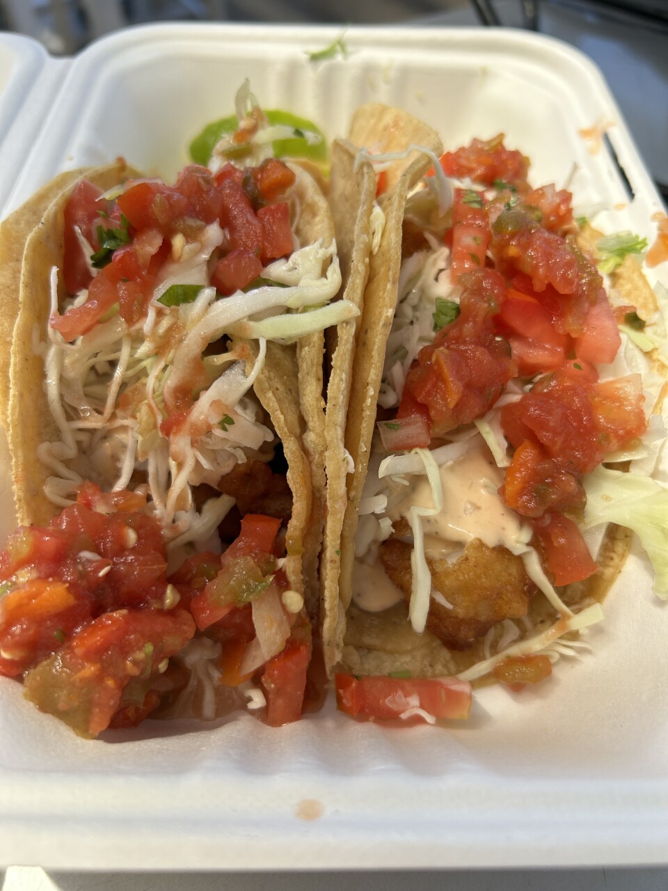 A close-up look at two fish tacos: It starts with full-size corn tortillas, then the tasty fish drizzled with chipotle sauce and topped off with cabbage and pico de gallo.