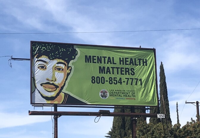 A billboard with a green background and the illutration of a mustachioed man reads: MENTAL HEALTH MATTERS 800-854-771