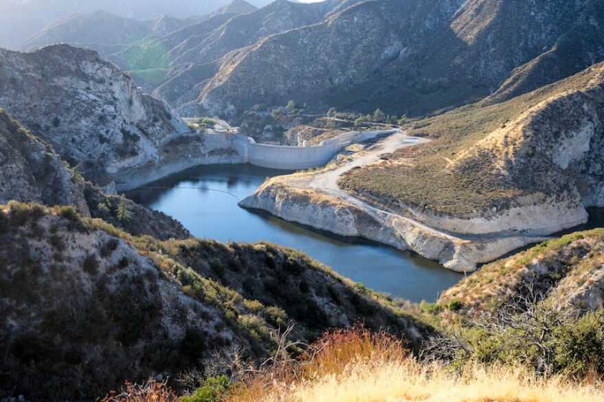 Photo of Tujunga Dam, surrounded by tree-covered hills, and a river winding through the center.
