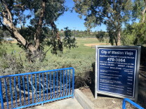 View from the top of a staircase overlooking a soccer field. A sign in the foreground reads "City of Mission Viejo" followed by park regulations.