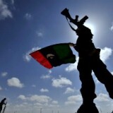 A Libyan anti-Kadhafi fighter waves the flag of the rebellion on a desert road some 30 kilometers from the eastern town of Brega on March 31, 2011.