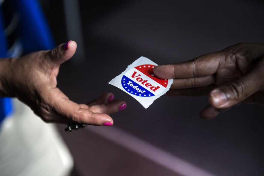 A poll worker hands out 'I Voted' stickers. 