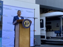 Congressman Tony Cárdenas speaks at a press conference Thursday, calling for additional federal and state funding for the new suicide and mental health crisis lifeline. Cárdenas wears a blue suit and to his right is a banner which has information for 988 -- the suicide and crisis lifeline. To his left is a white van that says 'Los Angeles County' on the door. It's one of L.A. County's therapeutic transport vans, which are staffed by unarmed teams who respond to mental health crises. 