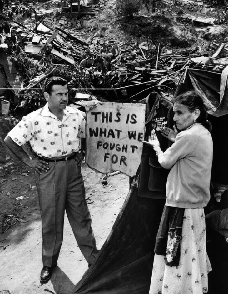 Two people stand near a pile of rubble with the sign: This is what we fought for.