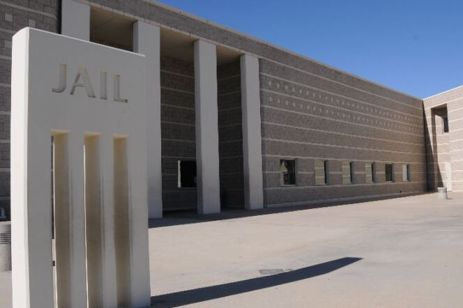 The exterior of a jail has the word "JAIL' carved into sign outside an empty courtyard expanse. The block walls have stripes and a row of first-floor windows