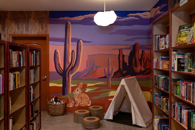 Filled bookstore shelves set against a painted wall mural of cacti, a bunny, a tent, and desert sunset.