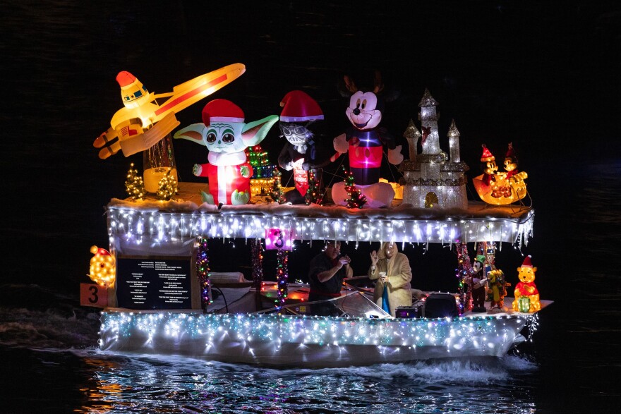 A boat floating in the water, decorated for the holidays. Inflatable versions of familiar characters are displayed, including Yoda, Mickey Mouse and Winnie the Pooh.