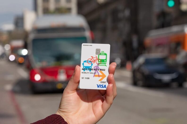 Closeup of a hand holding a white card for the Metro Mobility Wallet program. A red city bus is in the background.