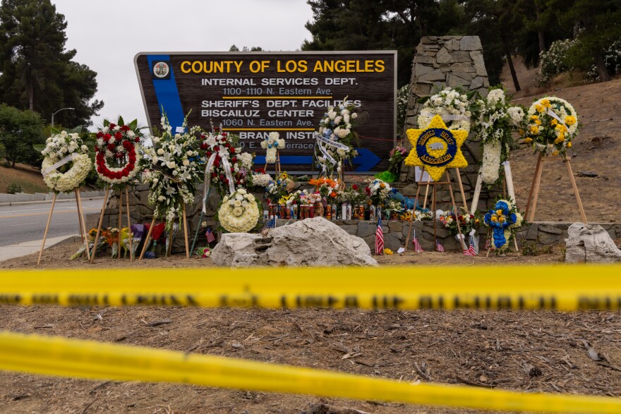 A sign reads "County of Los Angeles" is framed by several floral arrangements and candles.