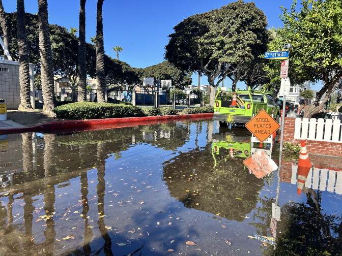 Floodwaters cover a street, with a utility truck and a 'Steel Plates Ahead' sign standing in the water.