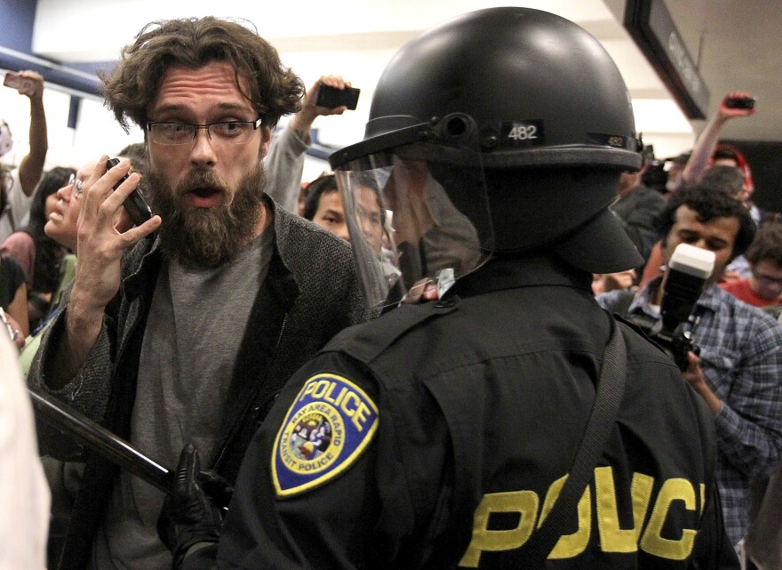 SAN FRANCISCO, CA - AUGUST 15:  A protestor pretends to talk on a cell phone as he taunts a Bay Area Rapid Transit (BART) police officer at the Civic Center station on August 15, 2011 in San Francisco, California.  The hacker group "Anonymous" staged a demonstration at a BART station this evening after BART officials turned off cell phne service in its stations last week during a disruptive protest following a fatal shooting of a man by BART police.  (Photo by Justin Sullivan/Getty Images)