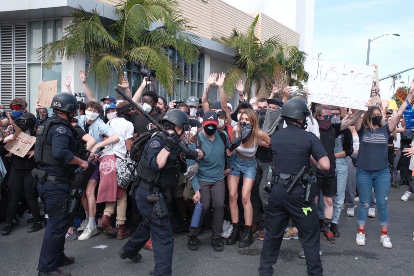 LAPD officers from the Metro squad met protesters with force. In this image the middler officers wields a long baton like a baseball bat and appears to be swinging forward at protesters, some of whom have their hands raised.