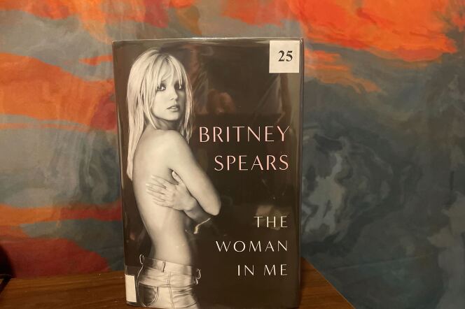 A physical library copy of Britney Spears's memoir "The Woman in Me" against an orange and blue backdrop.