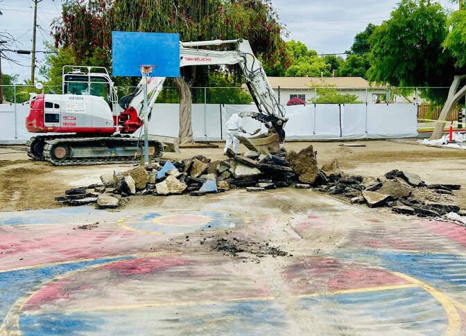 A backhoe next to a school yard, broken asphalt next to it.