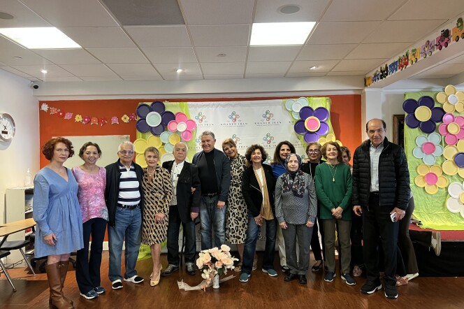 A group of people stand in front of a vase of flowers looking ahead. Behind them, is a backdrop of paper plate flowers. 