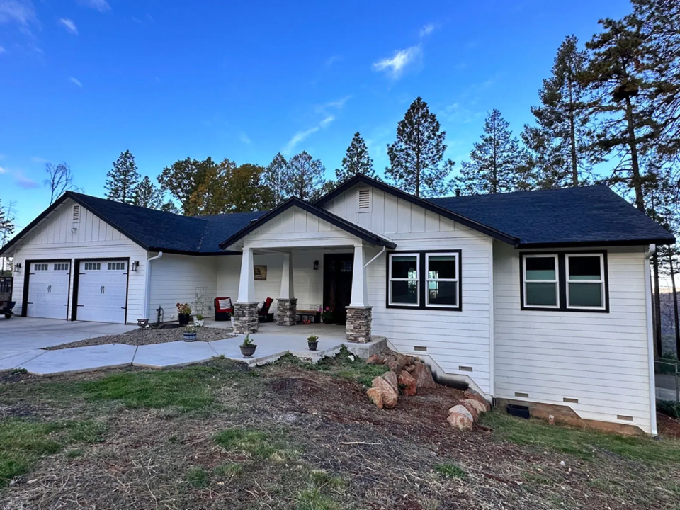 A newly built white clapboard home with a black slate roof and a two car garage