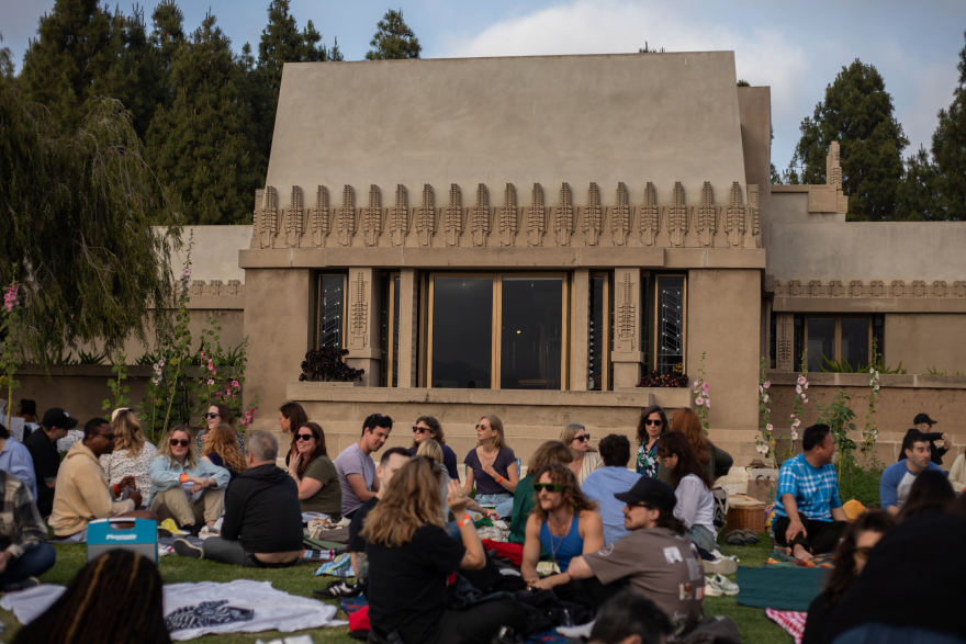 Groups of people sitting on the lawn and picknicking in front of an ornate cement building (Hollyhock House) in Barnsdall Art Park.