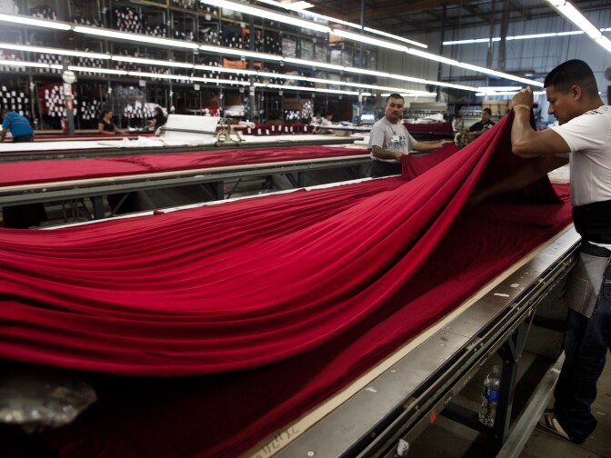 Antonio Herdandez, left, and Angel Guerrero spread fabric at the Karen Kane warehouse. The layered stack of fabric is then cut to make different components of the clothing.