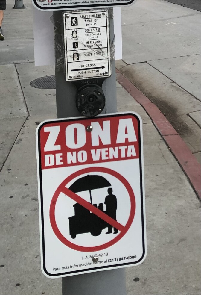 A sign that reads "No-vending zone" in Spanish with a photo of a street vendor crossed out by a red line.
