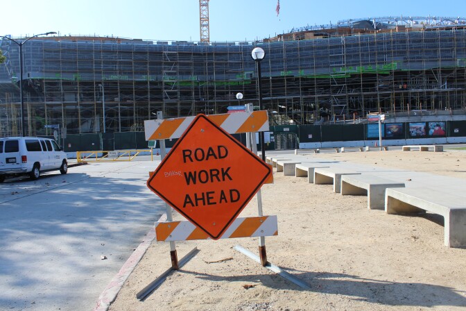 A bright orange "ROAD WORK AHEAD" sits next to a road, concrete benches, and in front of a big construction site - the future home of the Lucas Museum of Narrative Art