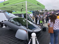 A silver vehicle with a sleek, futuristic design surrounded by a crowd. 