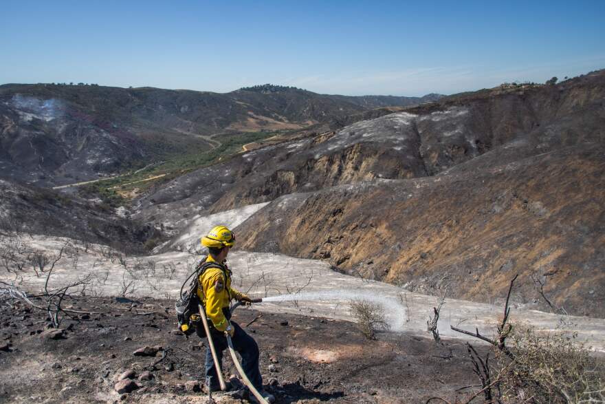 A firefighter sprays water on hotpots in a burned canyon behind homes destroyed by the Coastal Fire in Laguna Niguel, California.