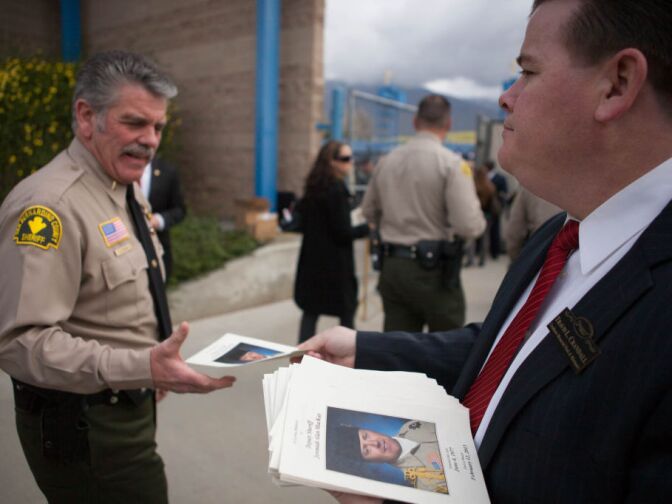 A funeral home employee passes out programs for the funeral of Det. Jeremiah MacKay in San Bernardino on Feb. 21, 2013.