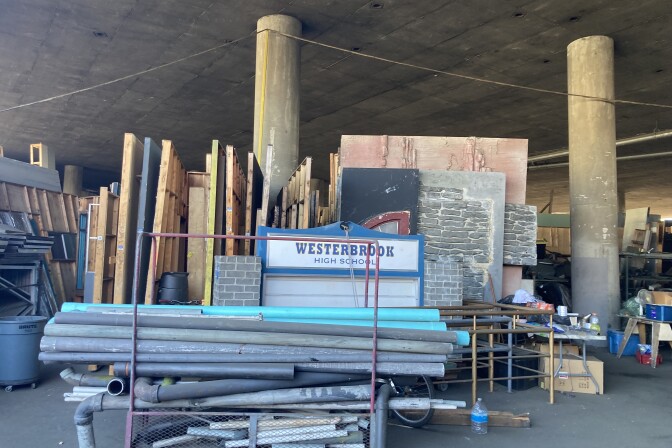 Pallets of wood, steel pipes and a sign that says "Westerbrook High" are piled at a set recycling company that operates under the 10 Freeway 