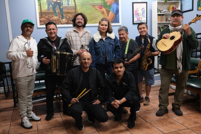 A woman stands with a group of men, some of whom are holding musical instruments.