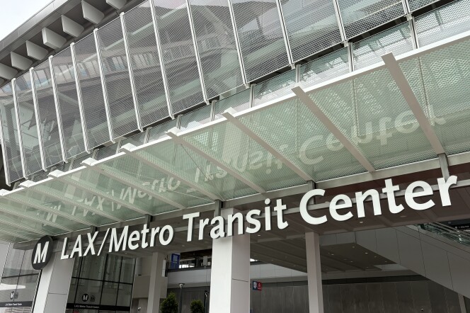 A black and white sign with an "M" representing L.A. Metro's logo followed by "LAX/Metro Transit Center" The sign reflects on the glass above it. 