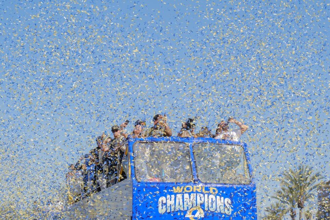 A double-decker bus and the people celebrating on top are nearly obscured by a cloud of confetti. The front of the bus reads "World Champions."
