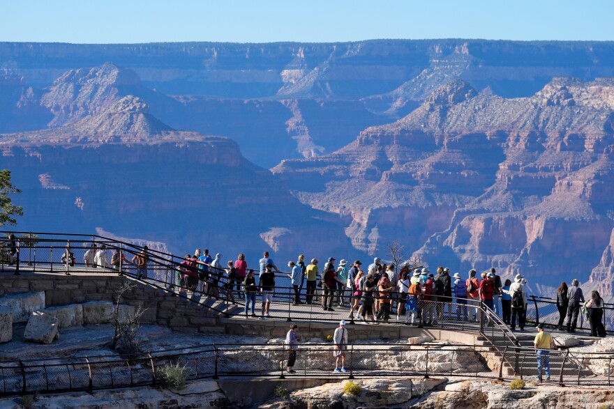 A crowd of people overlooking the Grand Canyon from a walkable area with rails.