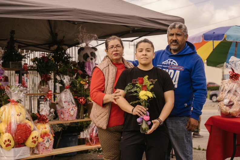 A family, a man and woman and daughter stand in front of their flower stand