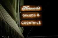 A nighttime view of Hermon’s neon sign reading “Dinner & Cocktails” glowing against the dark exterior.