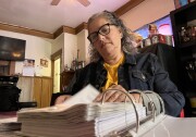 Cristina Campos sits at her family's kitchen table and flips through a binder of paperwork related to her apartment of 23 years.