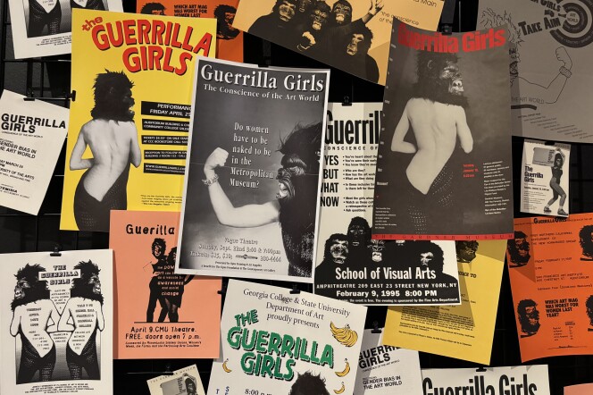 White, orange and yellow flyers pinned to a board with text that includes "Guerrilla Girls" and images of partially nude women wearing gorilla masks.