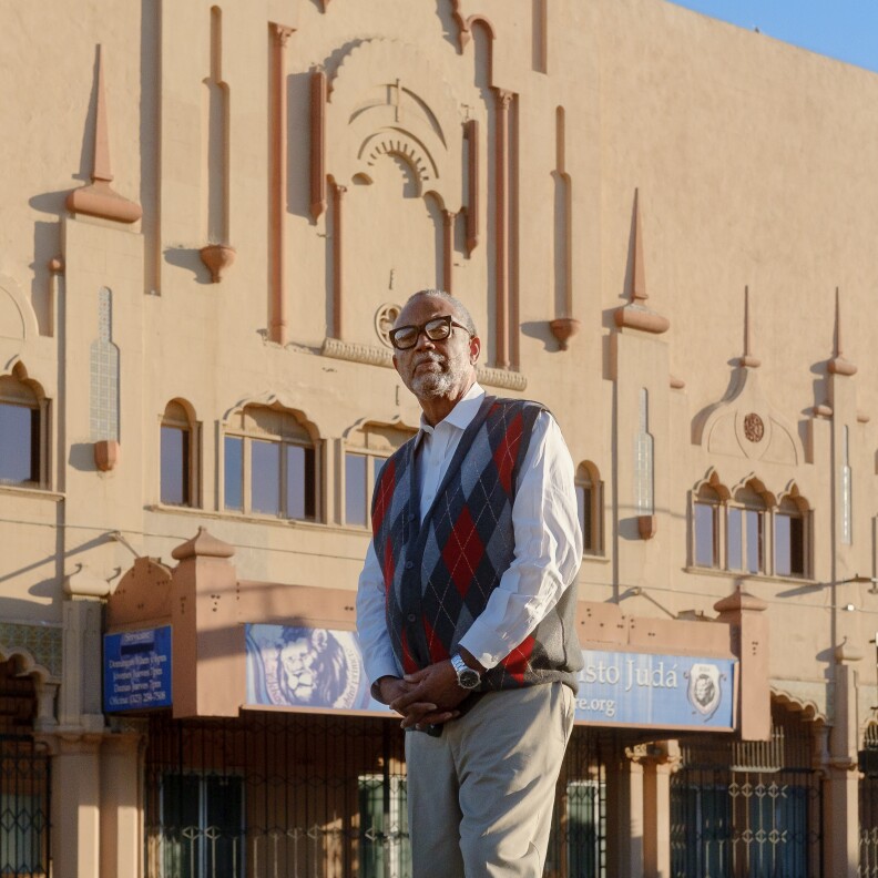 L.A. City Councilmember Curren Price stands in front of the Lincoln Theater located in his district. He's wearing a collared button down long-sleeved shirt with a sweater vest and tan slacks.