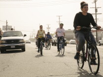 On a sunny, hazy day, a group of cyclists rides down a street.
