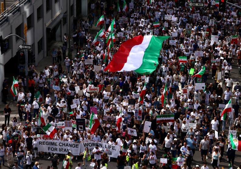A massive red white and green flag is carried by protesters who pack downtown streets