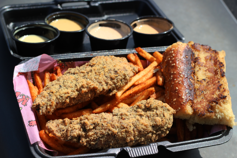 fried chicken tenders sit on a bed of seasoned orange fries next to a piece of grilled toast