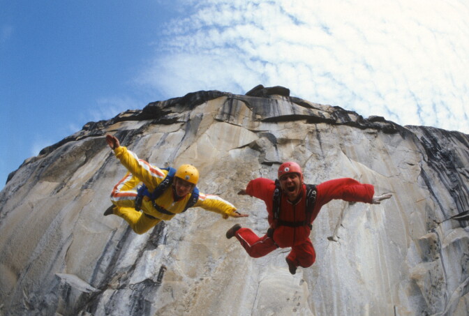 Jean and Carl Boenish in jump down a ledge towards camera.