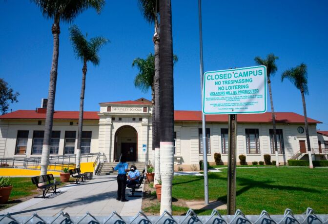 Two security guards talk on the campus of the closed McKinley School, part of the Los Angeles Unified School District (LAUSD) system, in Compton, California, just south of Los Angeles, on April 28, 2020. - California may start the new school year as early as July to make up for some of the "learning loss" due to the pandemic, the state's Governor Gavin Newsom said on April 28. (Photo by Robyn Beck / AFP) (Photo by ROBYN BECK/AFP via Getty Images)