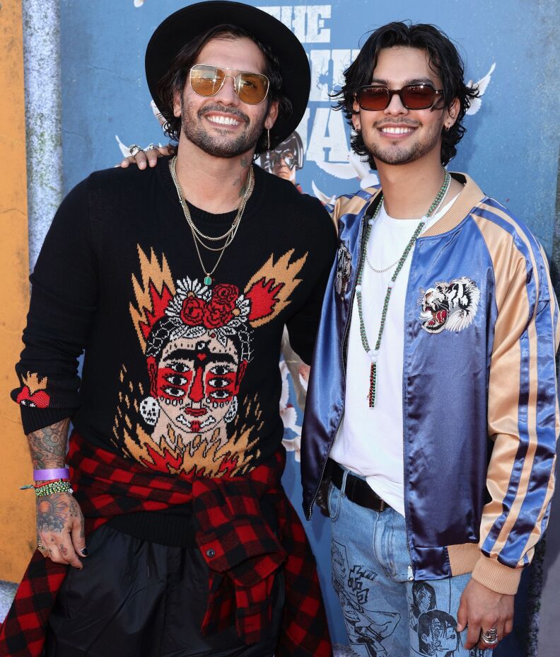 Two men in colorful casual clothes stand arm-in-arm.