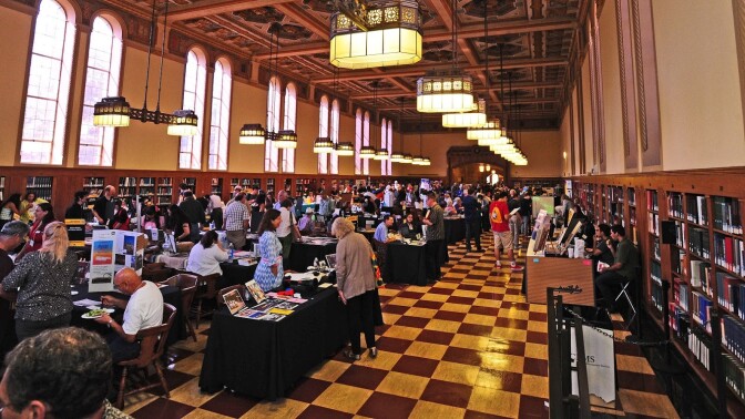 A library hall is filled with table and vendors presenting archival work to patrons.